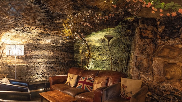 Un intérieur chaleureux avec un mur en pierre, un canapé en cuir agrémenté d’un coussin orné du drapeau britannique, une table basse en bois et une lampe.