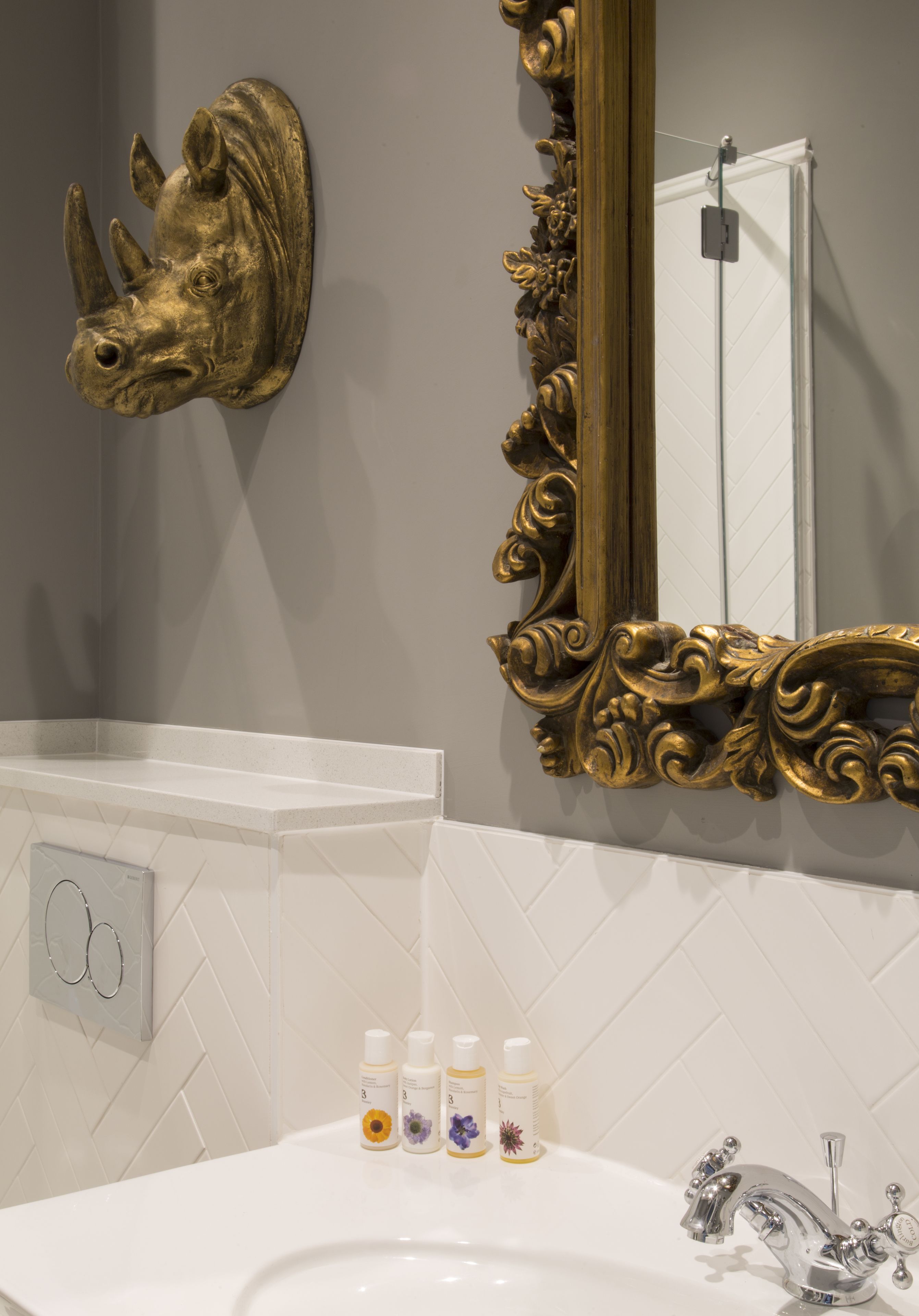 A bathroom with a white sink, a gold mirror, and a rhinoceros head decoration on the wall.