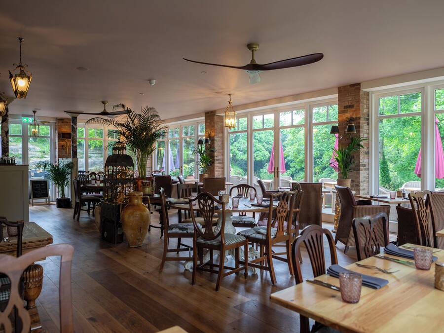 A spacious indoor dining area with wooden tables and chairs, large windows, and ceiling fans.