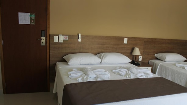 Habitación de hotel con dos camas, cabecero de madera, mesita de noche con lámpara y puerta con lector de tarjeta.