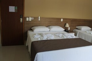 A hotel room with two beds, a wooden headboard, a bedside table with a lamp, and a door with a keycard reader.