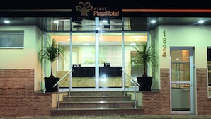 Exterior del hotel Avaré Plaza, con entrada de vidrio, dos plantas en macetas y fachada de ladrillo.