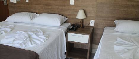 A hotel room with two beds, a bedside table with a lamp, a phone, and a drawer.