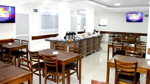 Un restaurante con mesas y sillas de madera, un mostrador de buffet y televisores mostrando menús.