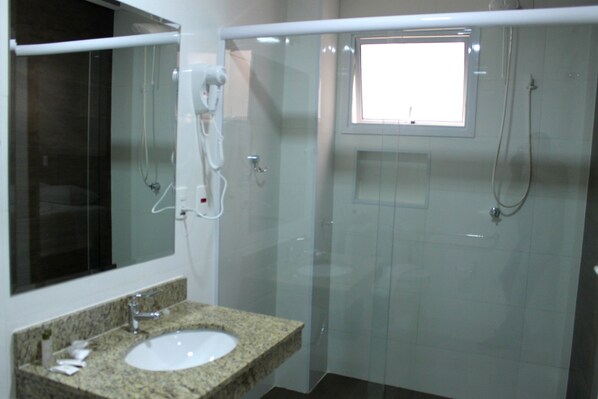 A bathroom with a granite countertop sink, a mirror, a glass shower enclosure, and a window.