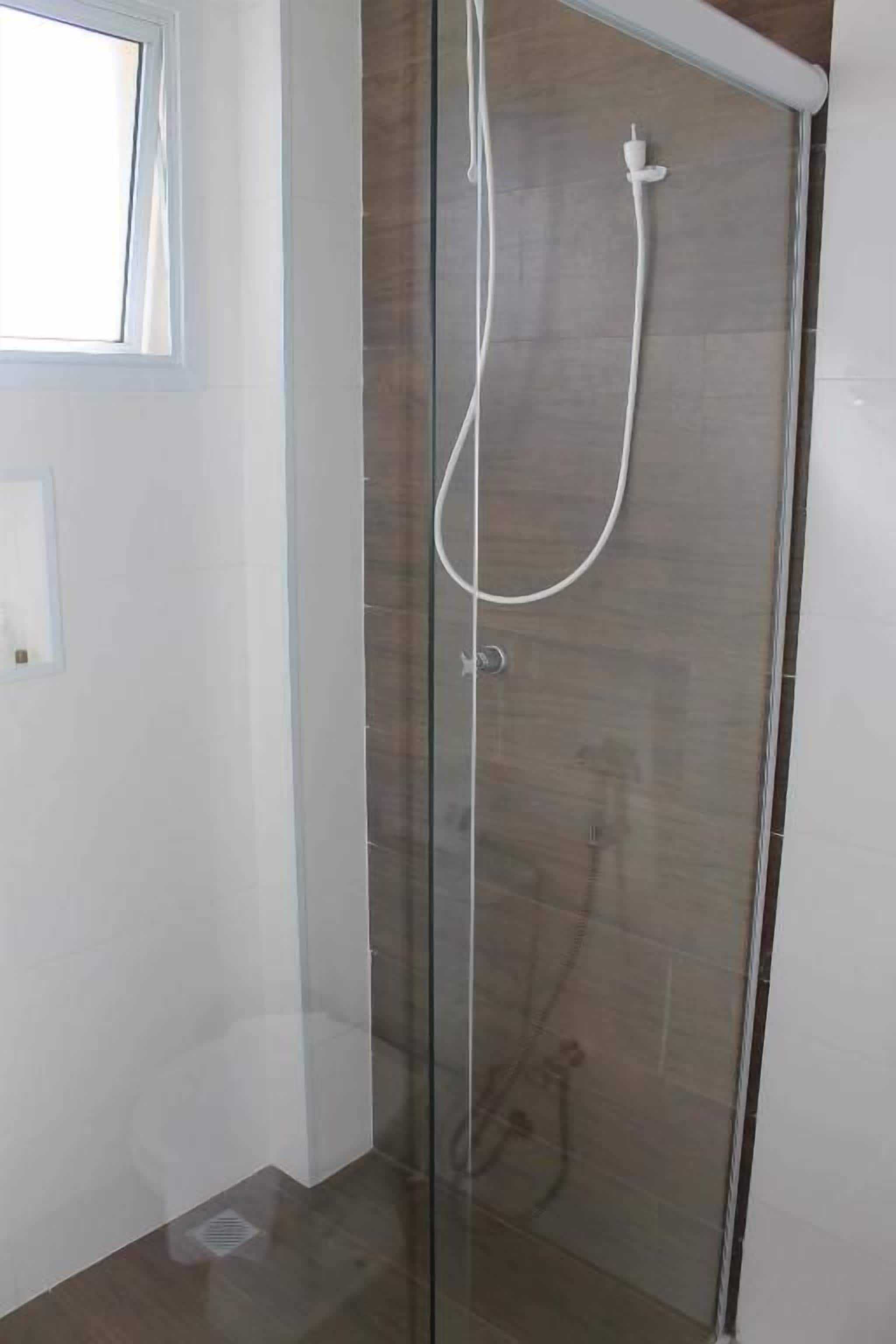 A glass-enclosed shower with a handheld showerhead and a wall-mounted faucet.