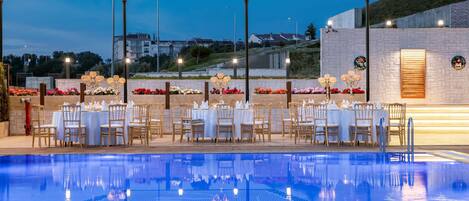 A poolside dining area with tables and chairs, surrounded by a pool with clear blue water.