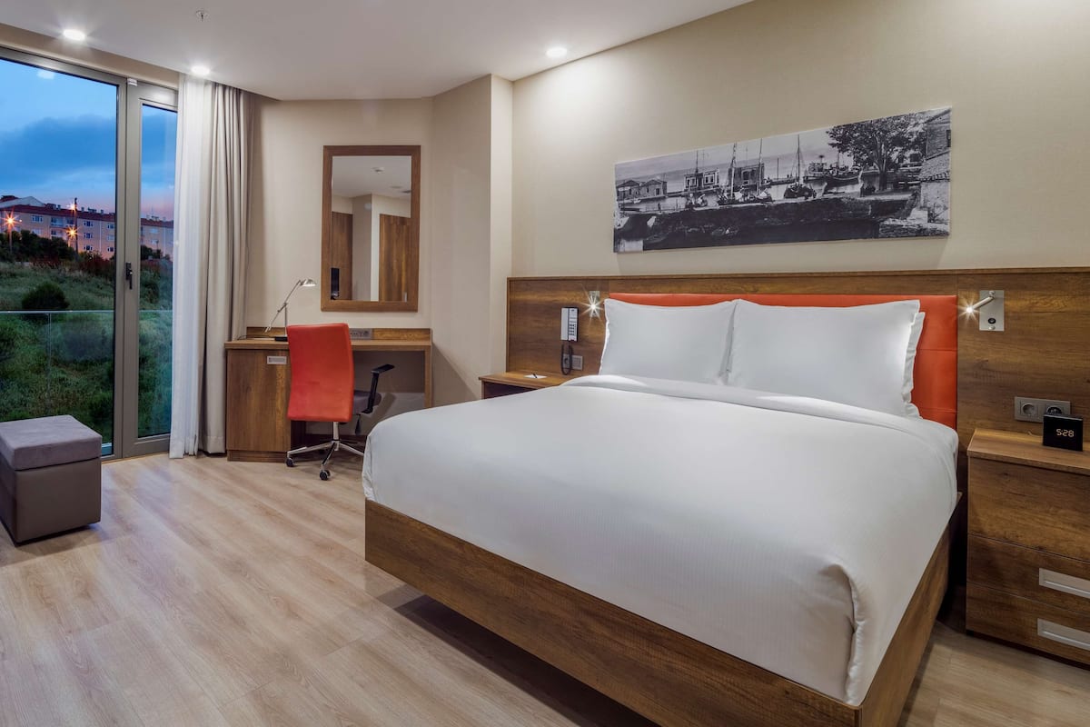 Habitación de hotel con una cama grande, un escritorio, una silla, una mesita de noche, un teléfono, un reloj y un cuadro en la pared.