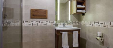 A bathroom with a shower, sink, and toilet. There is a towel rack with two towels, a wooden medicine cabinet, and a mirror above the sink.