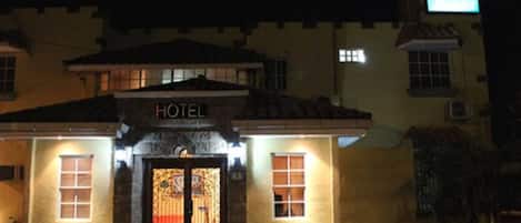 A hotel with a sign above the entrance, a tiled roof, and a lit-up signboard.
