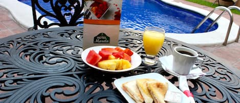 A dining table with a menu, a plate of fruit, a glass of orange juice, a cup of coffee, and a sandwich.