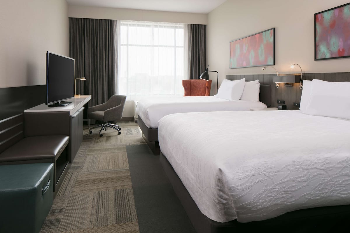 A hotel room with two beds, a desk with a flat-screen TV, a chair, and a desk lamp.