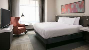 Habitación de hotel con una cama grande, un escritorio, un televisor de pantalla plana, una silla, una mesita de noche y una ventana con cortinas.