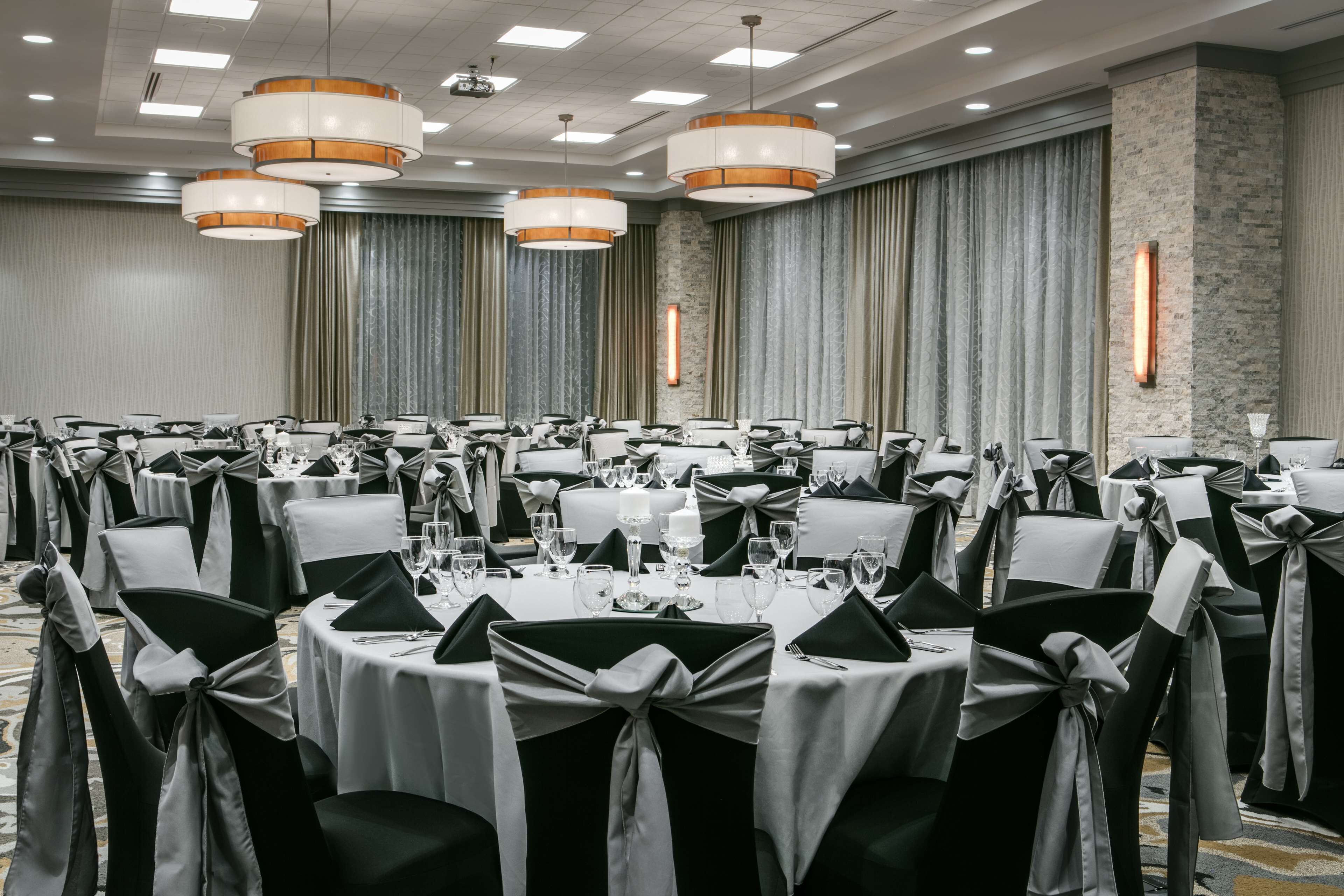 A banquet hall with round tables, black and white chairs, and overhead lighting.