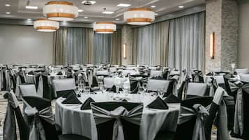A banquet hall with round tables, black and white chairs, and overhead lighting.