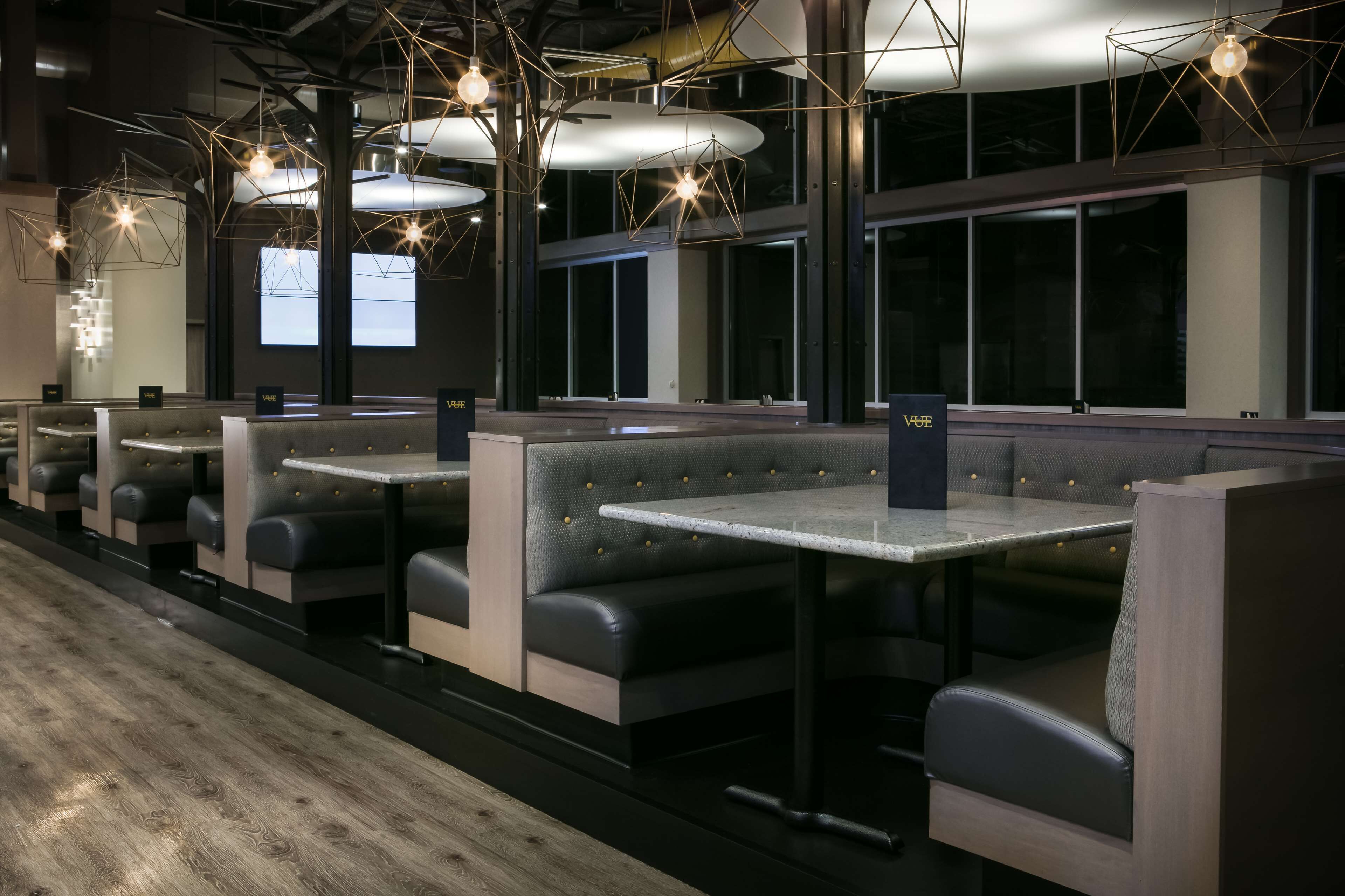 A modern restaurant interior with booth seating, pendant lighting, and a view of the city through large windows.