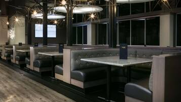 A modern restaurant interior with booth seating, pendant lighting, and a view of the city through large windows.