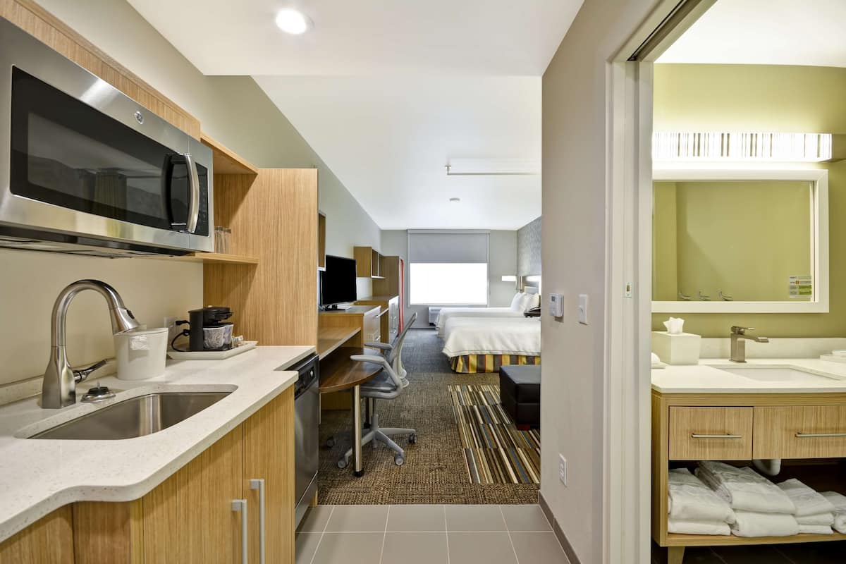 A modern hotel room with a kitchenette, a large bed, a separate bathroom, and a view of the city.