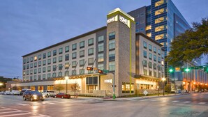 Un hotel moderno con un llamativo letrero que dice “HOME”, un estacionamiento y la intersección de una calle.