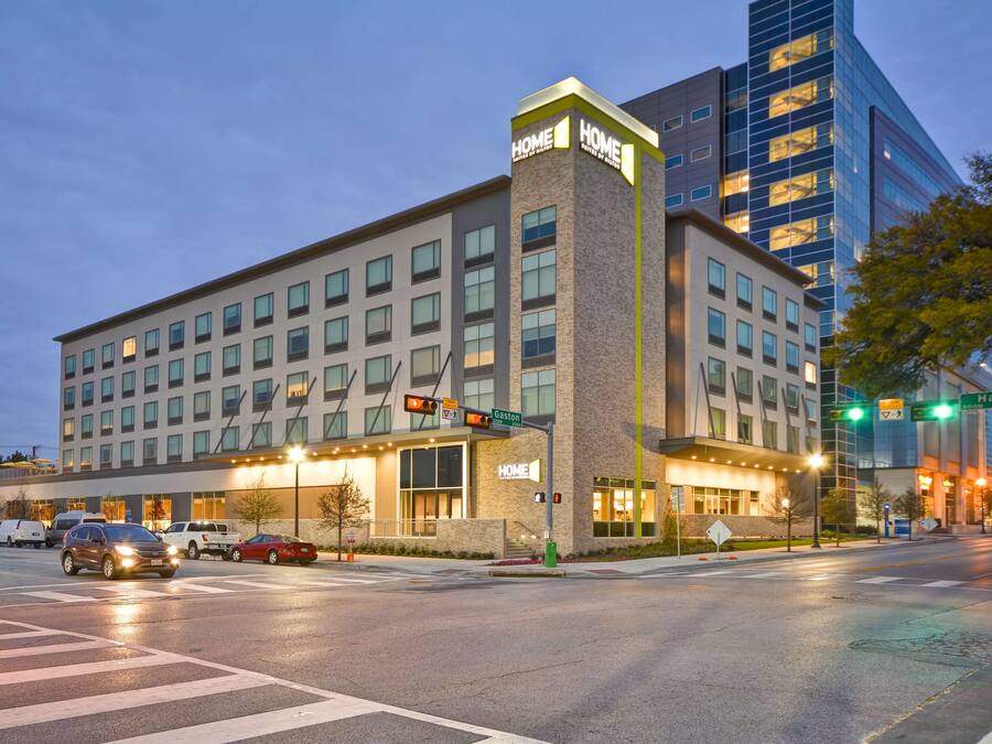 Un hotel moderno con un llamativo letrero que dice “HOME”, un estacionamiento y la intersección de una calle.