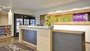 A hotel reception area with a counter, a fruit display, a minibar, and a snack shelf.