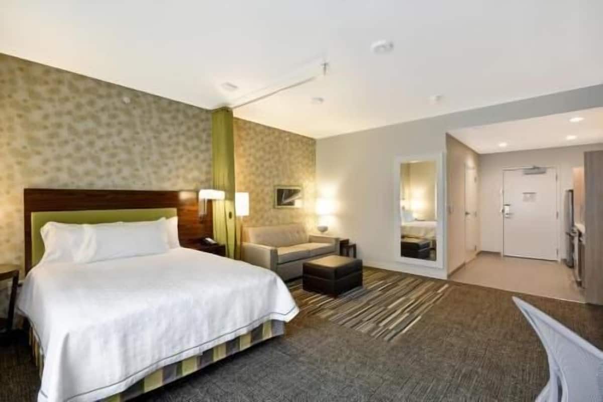 A hotel room with a bed, a sofa, a small table, a mirror, and a door.