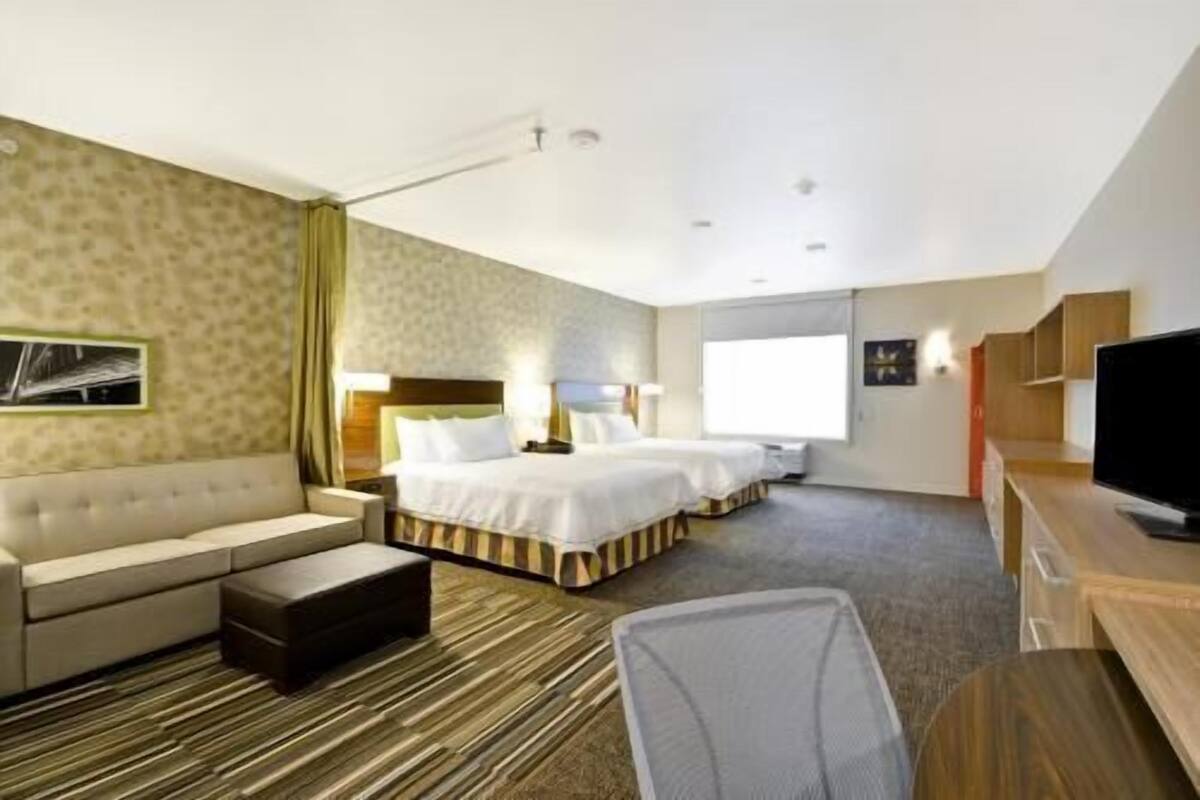 A hotel room with a sofa, two beds, a TV, and a desk.
