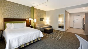 Una habitación de hotel con una cama grande, un sofá, una mesita y un espejo.