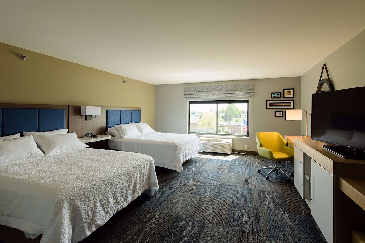 A hotel room with two beds, a desk with a TV, a chair, and a window with a view of the outdoors.