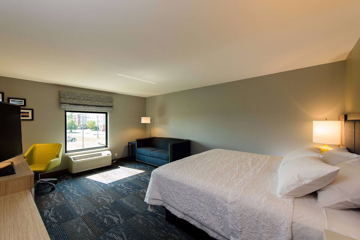 A hotel room with a bed, a desk, a chair, a window, and a radiator.