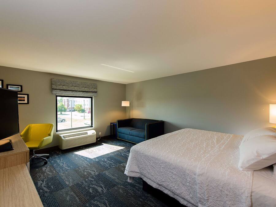 Une chambre d’hôtel avec un lit, un bureau, une chaise, une fenêtre et un radiateur.