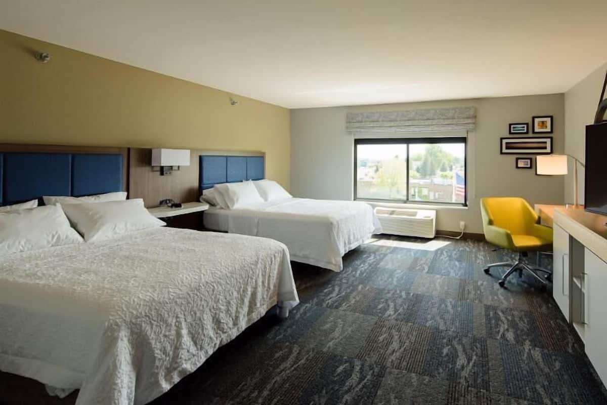 A hotel room with two beds, a desk with a chair, a window with a view, and a flat-screen TV.