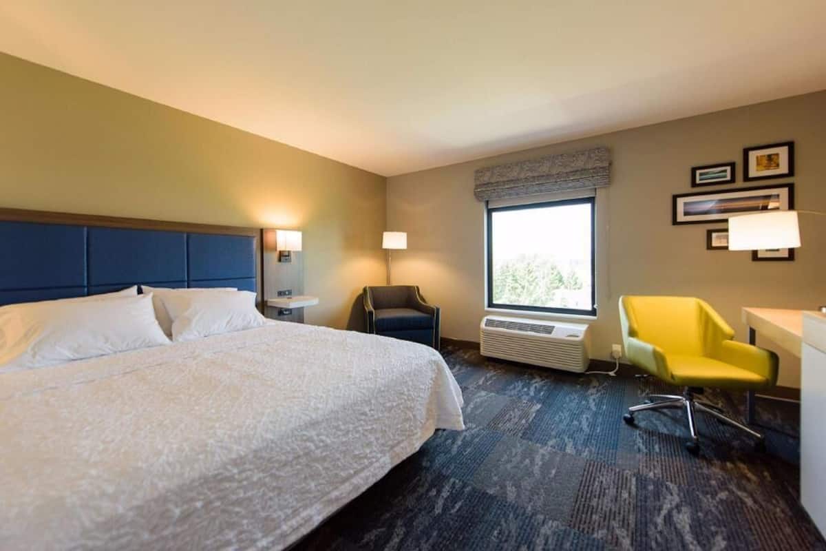 A hotel room with a bed, a desk, a chair, a window, and wall-mounted lamps.