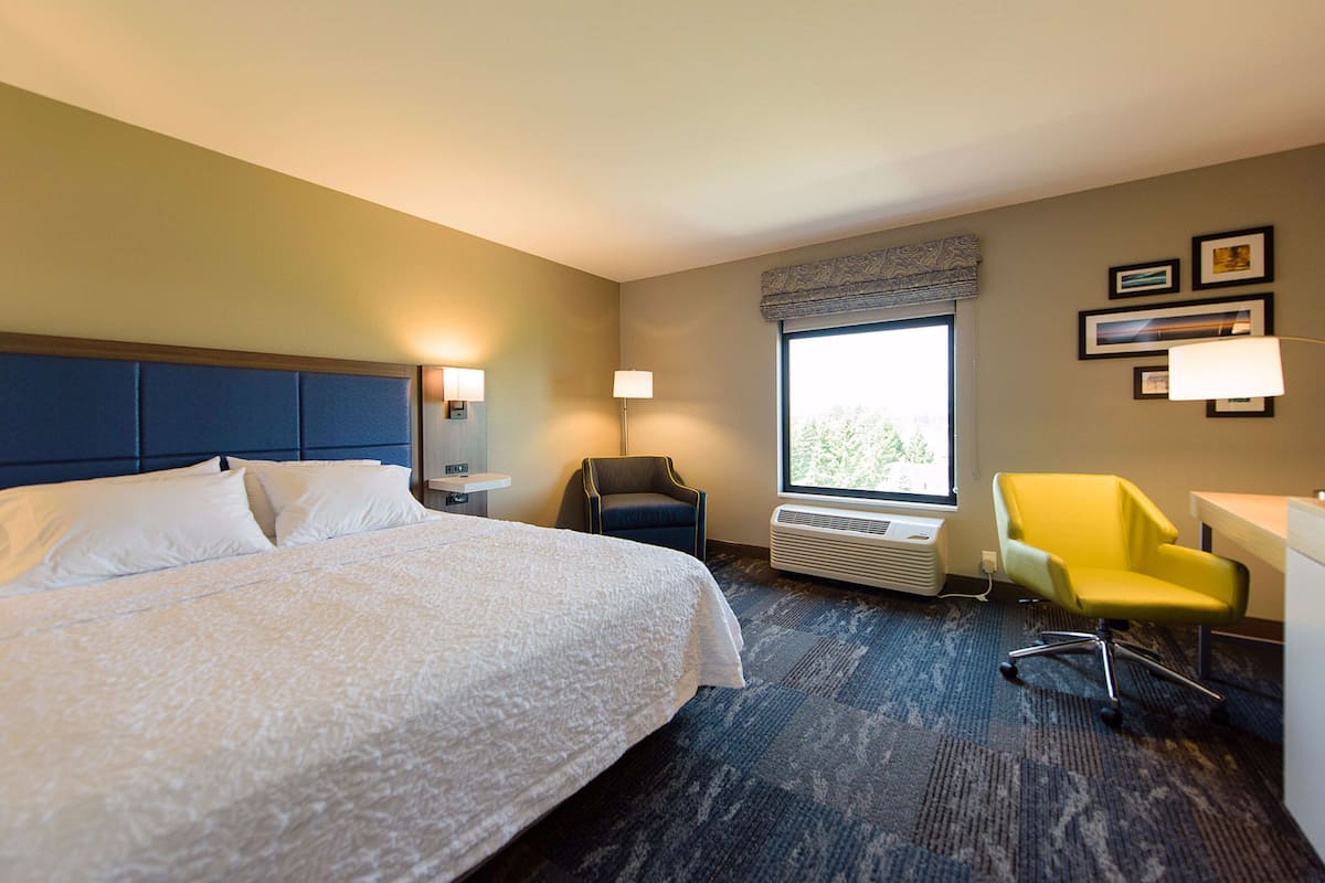 A hotel room with a large bed, a desk, a chair, a window, and wall-mounted lamps.
