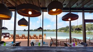 Un área de comedor al aire libre con mesas y sillas, grandes lámparas colgantes y vistas a un lago.