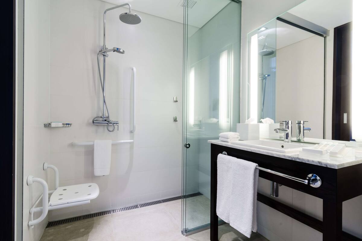 Une salle de bain moderne avec une douche à l’italienne, un meuble-lavabo doté d’un grand miroir et une serviette blanche posée sur le plan de travail.
