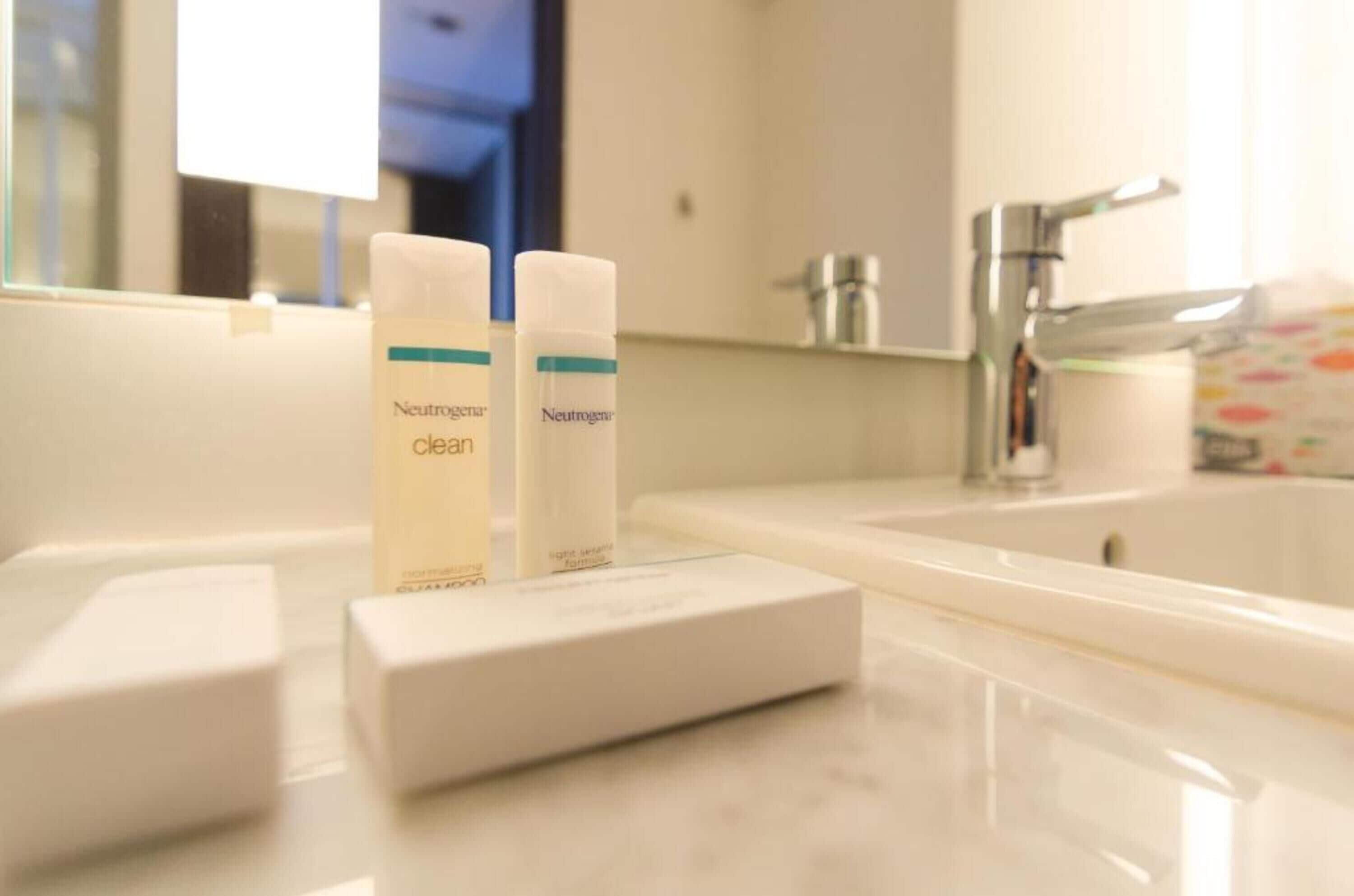 A bathroom with a white sink, two bottles of Neutrogena Clean Skin Moisturizing Lotion, and a white soap dish.
