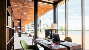 Un espacio de oficina moderno con un escritorio de madera, computadora y silla verde. Cuenta con ventanas grandes que ofrecen vistas a edificios y una masa de agua.