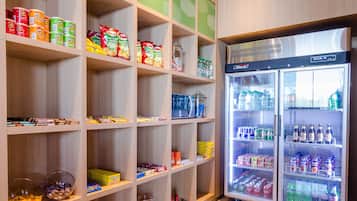 Zona de exhibición de aperitivos y bebidas con estantes llenos de diversas opciones y un refrigerador.