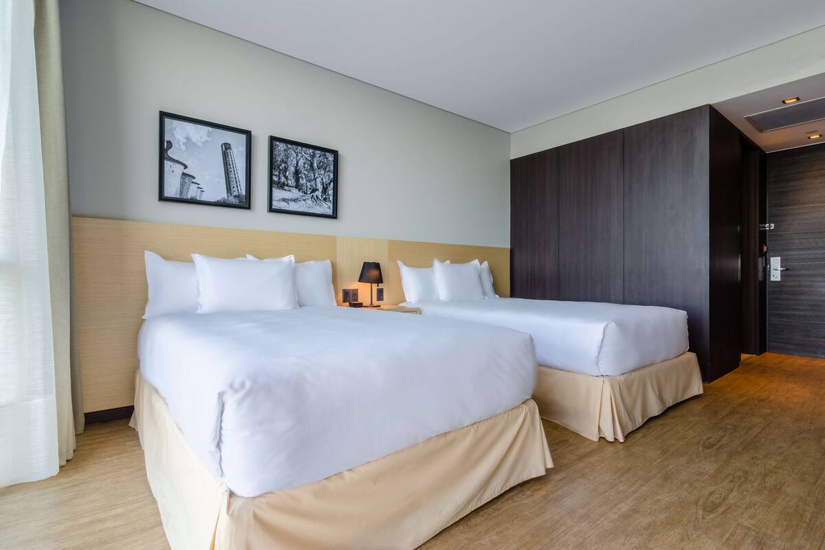 Une chambre d’hôtel avec deux lits, une tête de lit en bois, une armoire sombre et deux tableaux encadrés accrochés au mur.