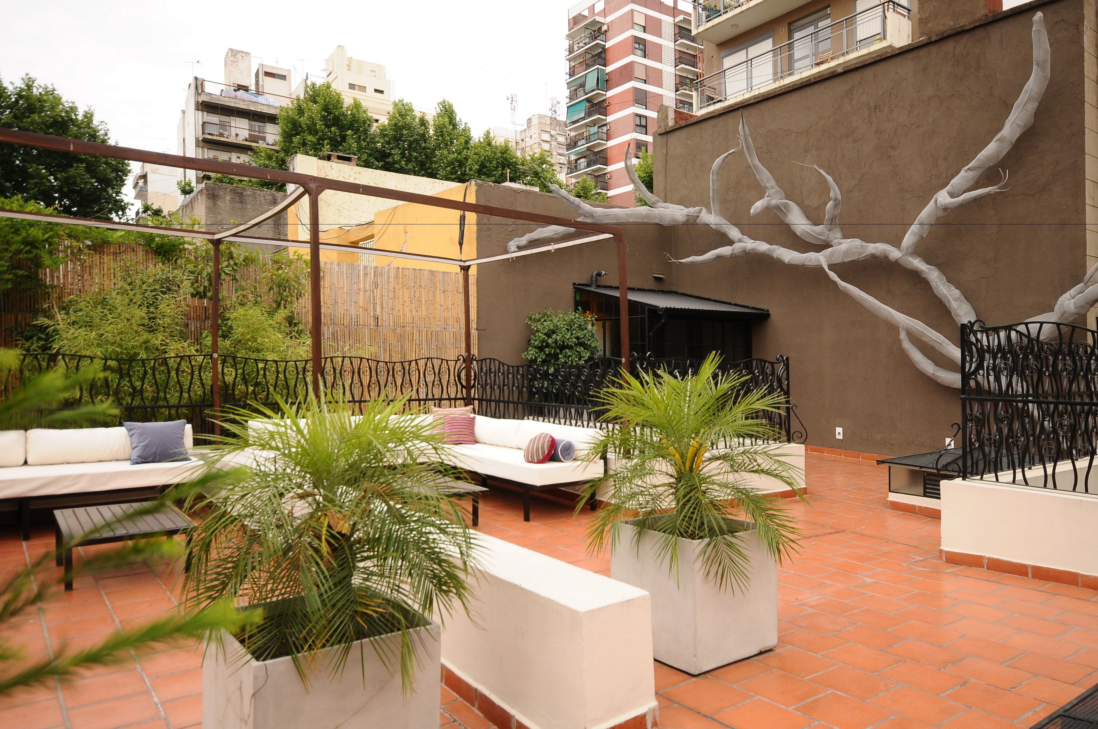 Un patio al aire libre con un sofá blanco, un banco y macetas con plantas.