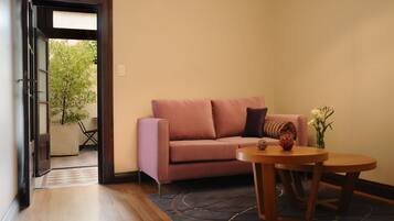 A room with a pink sofa, a round wooden table, and a vase with flowers.