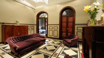 Una habitación con un sofá púrpura con capitonado, un sillón a juego, un armario de madera y un suelo de baldosas con un diseño geométrico.