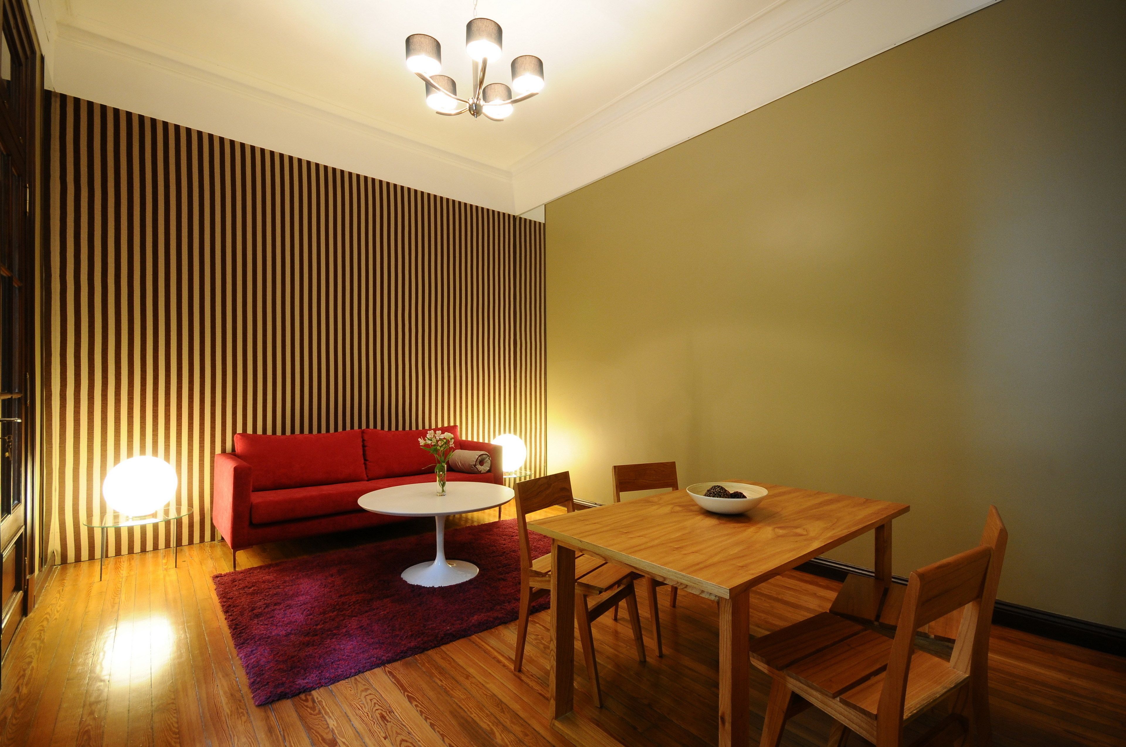 A modern living room with a red sofa, a round coffee table, and a wooden dining table with chairs.