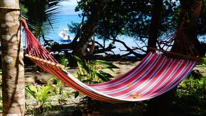 A hammock tied between trees in a tropical setting with a view of the sea. - Cebaco Sunrise Lodge (Isla Cebaco)