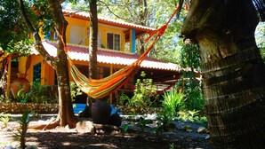 A hammock tied between trees in front of a colorful house with a tiled roof. - Cebaco Sunrise Lodge (Isla Cebaco)