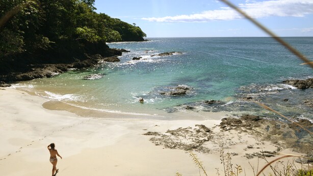 A beach with clear turquoise water, a sandy shore, and a person walking. - Cebaco Sunrise Lodge (Isla Cebaco)