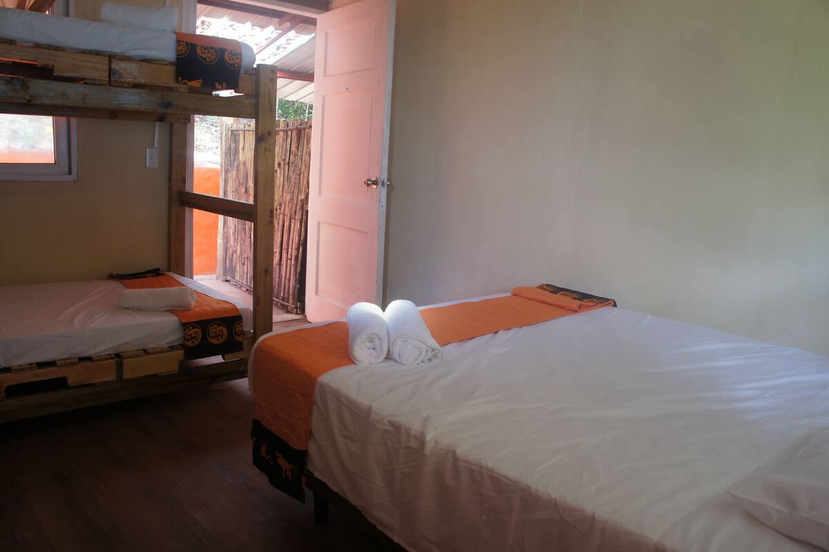 A dormitory room with bunk beds, a single bed, and a door leading to an outdoor area.