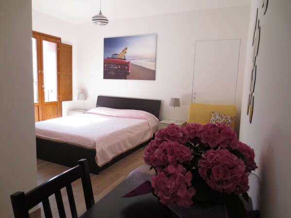 Una camera da letto con un letto, comodini, una lampada, un quadro, una porta e una sedia.