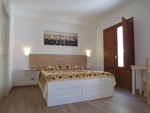 Una camera da letto con un letto, un comodino, una lampada a parete, una porta in legno e un tavolino.